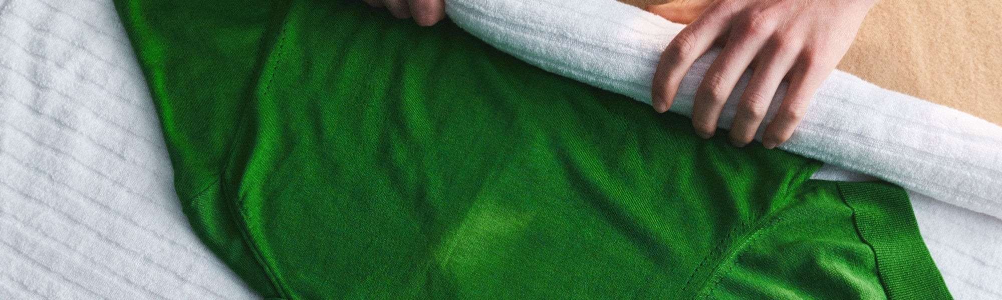 A green sweater being handled with a towel in Woolmark's sweater-care guide.