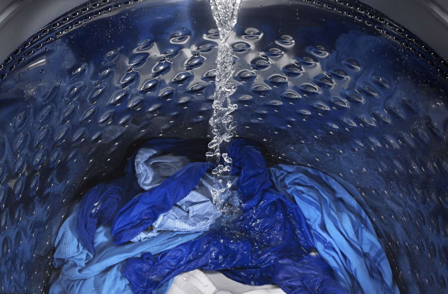 Blue laundry inside a washer receiving water in the source sweat-stain guide.