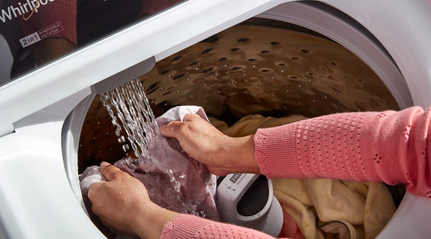A garment being rinsed under a washer faucet in the source oil-and-grease guide.
