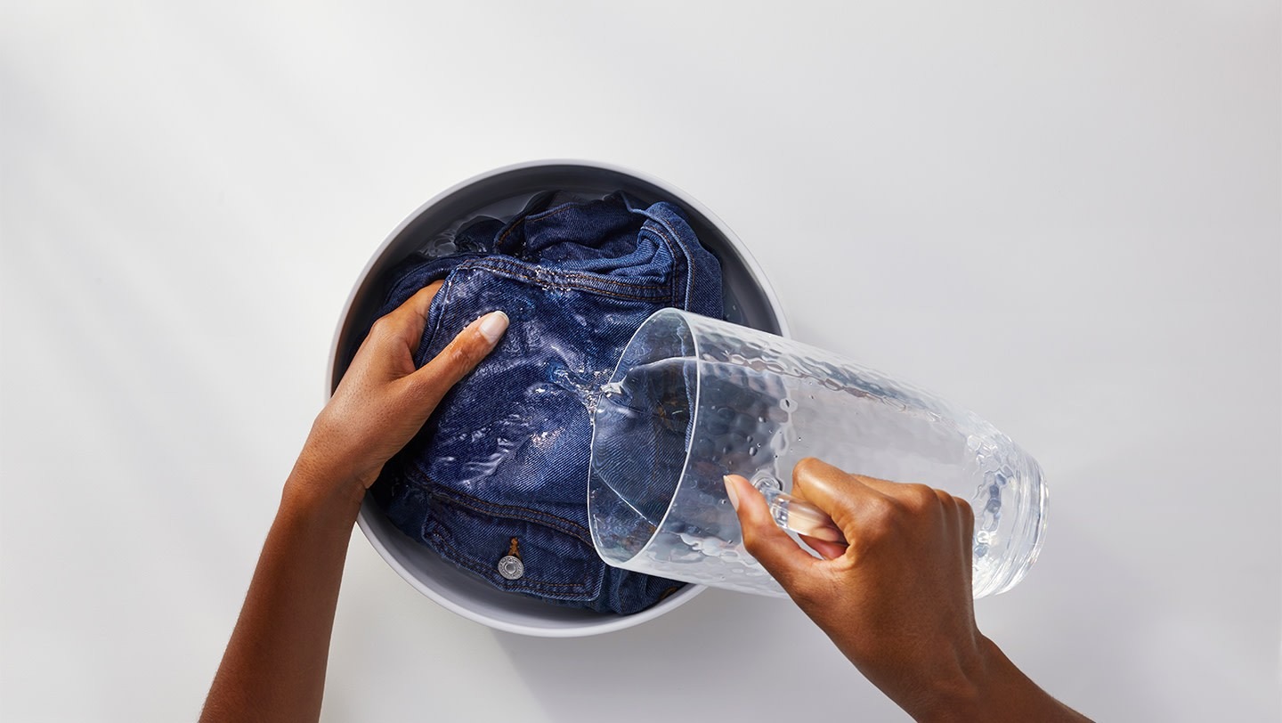 Water being poured over a denim garment in a basin in the source ink-stain guide.