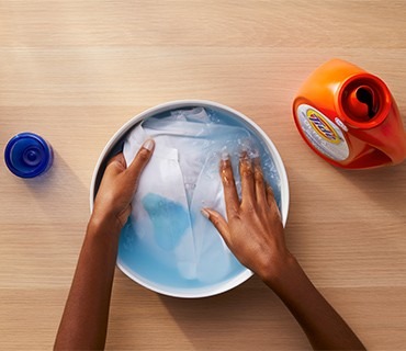 A lightweight garment being handled in a basin of water in the source delicate-care guide.