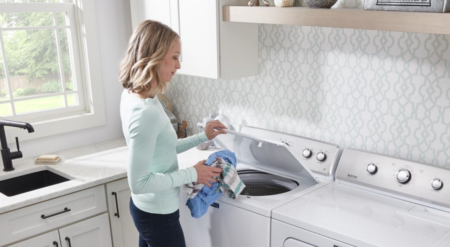 A person holding clothing beside a top-loading washer in the source makeup-care guide.