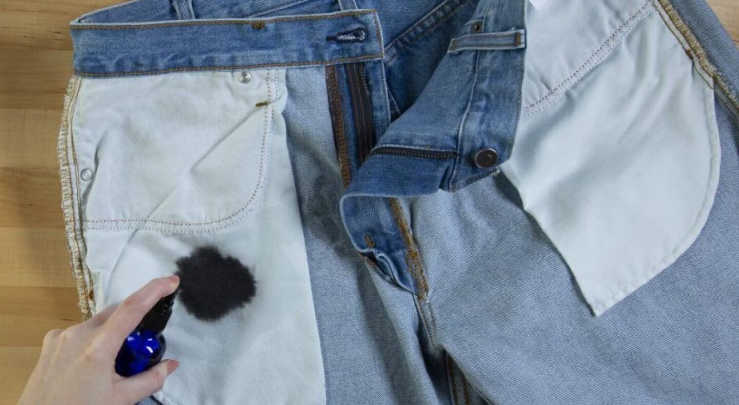 A dark ink mark on the inside of jeans beside a treatment bottle in the source ink-removal guide.