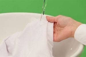 A white garment held under running water in the source wool-care guide.